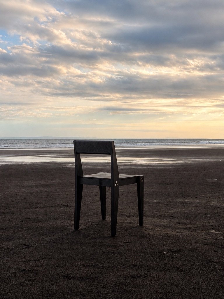 The Chair from behind on a dark sand beach at dusk, the sea and a cloudy sky beyond