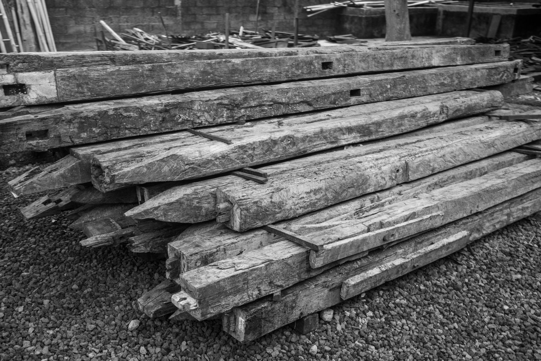 Old house beams stacked on gravel, with the joinery holes from their first life still in them