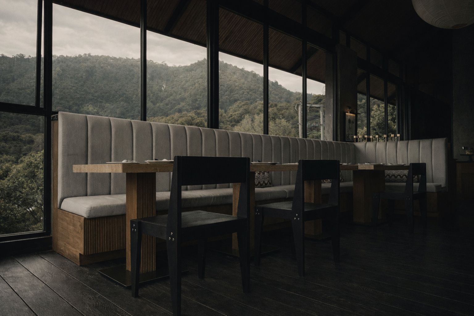 The Chair at restaurant tables beside a long upholstered banquette, forested hills through floor-to-ceiling windows.