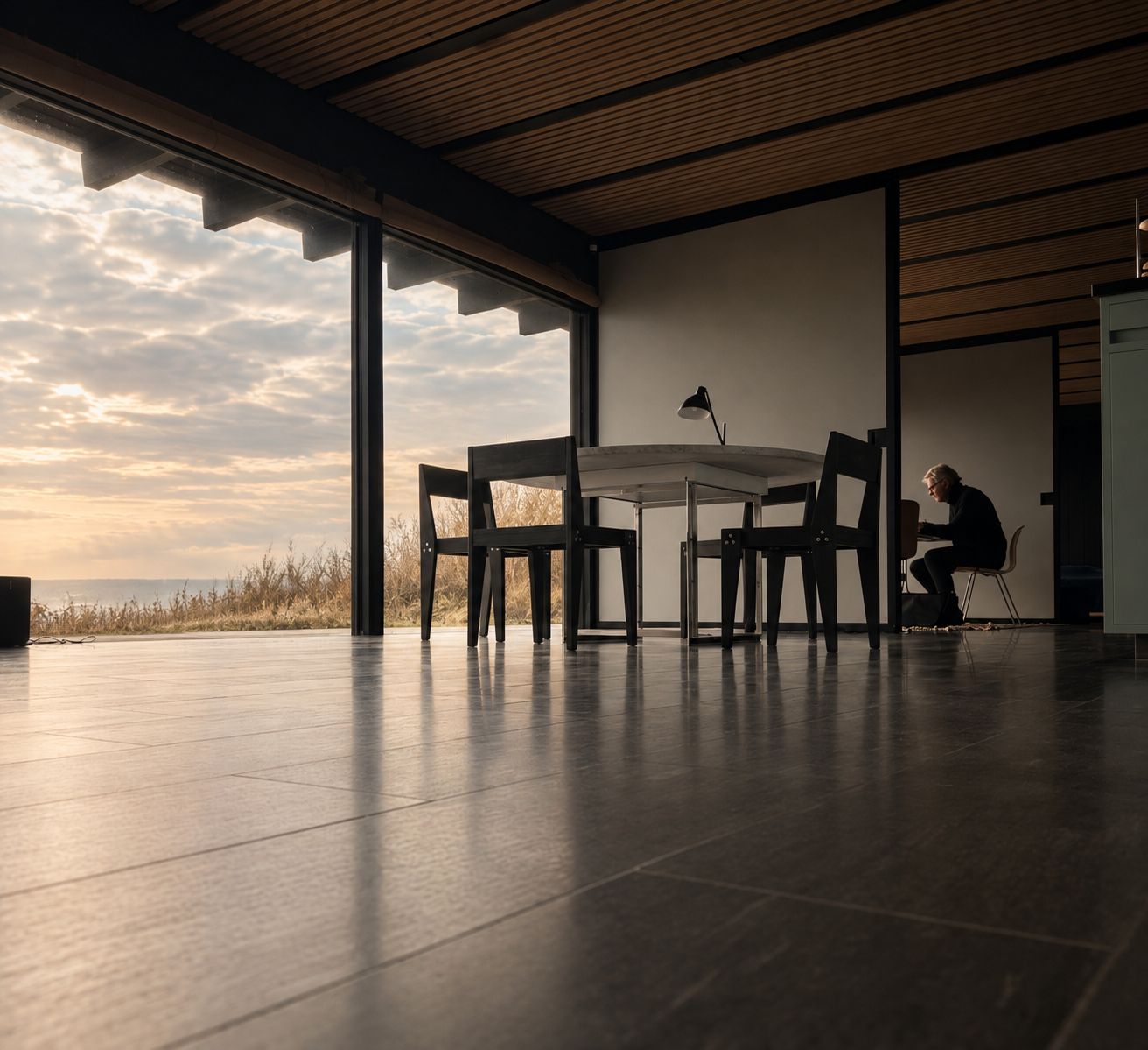 Chairs around a round table in a house by the sea, evening light across a stone floor.