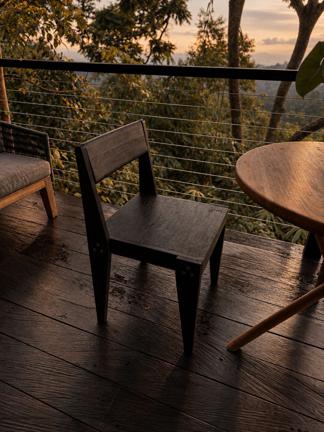 The Chair on a rain-wet timber terrace above the jungle at sunset, next to a round teak table.