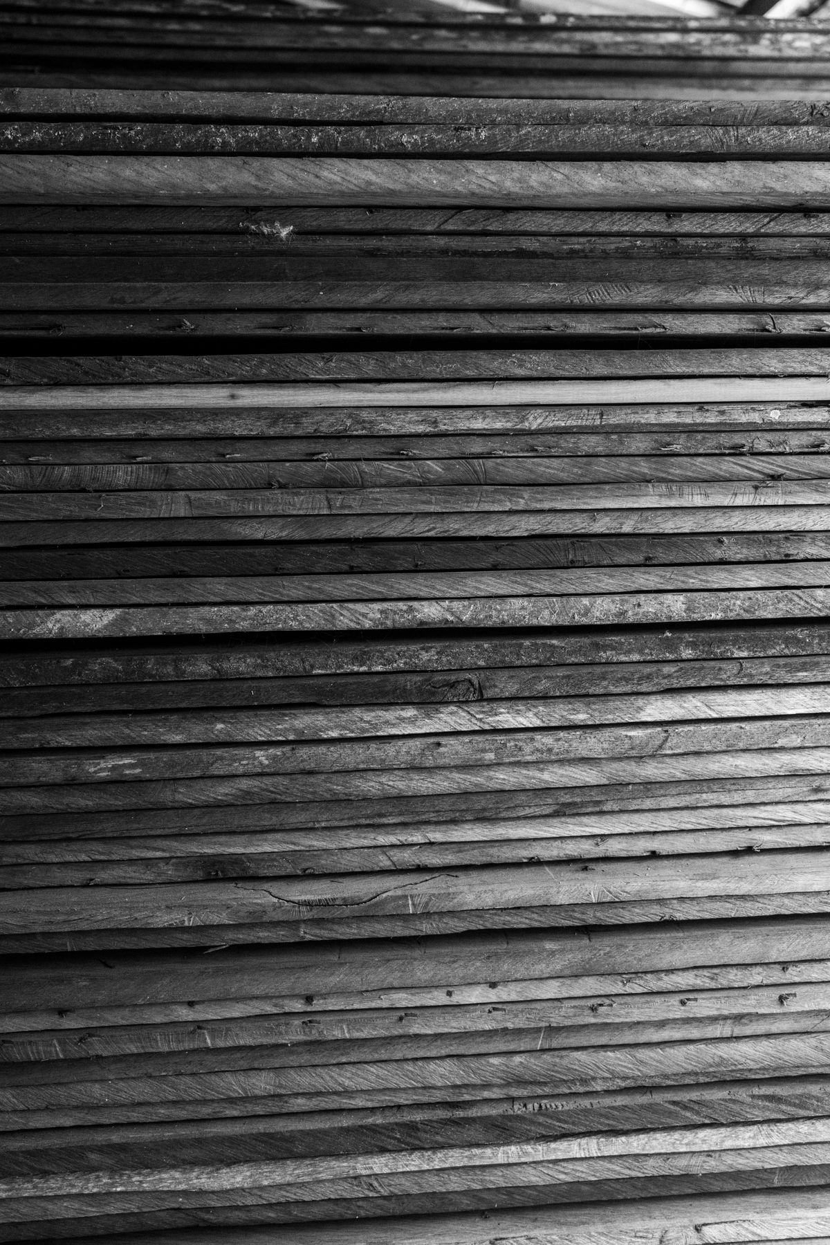 Close-up of stacked repurposed teak boards, with old nail holes, cracks and saw marks along their edges