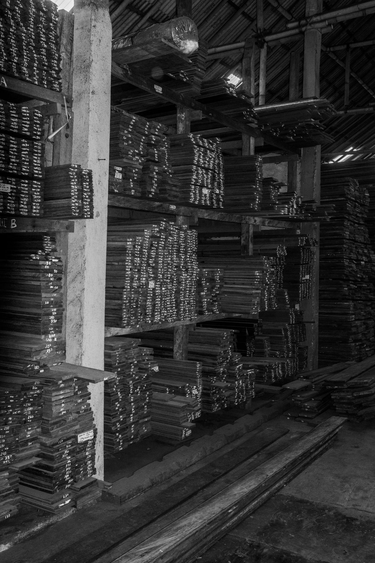 Racks of sorted teak boards in a timber store, each board marked by hand with its length